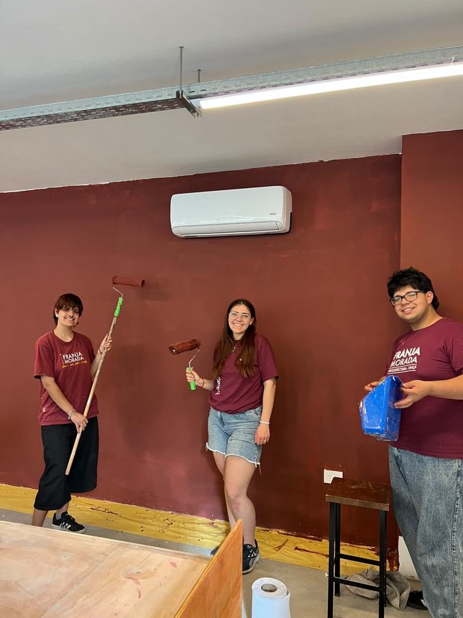 Militantes pintando una pared bordó del Centro con rodillos
